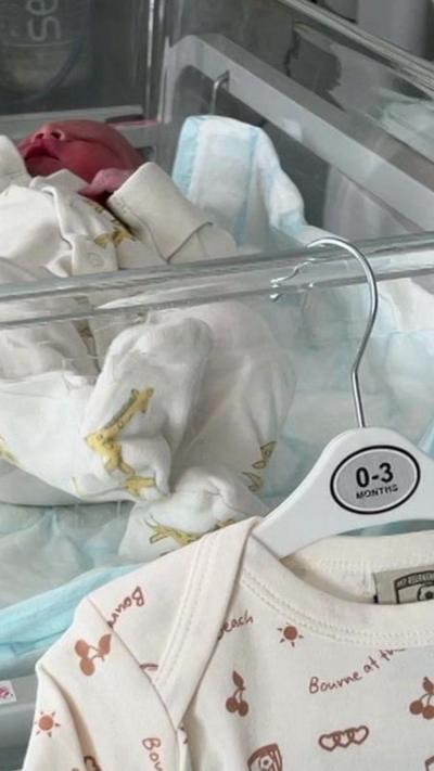 Baby sleeps in a clear cot in hospital with an AFC Bournemouth sleepsuit hanging on the side.