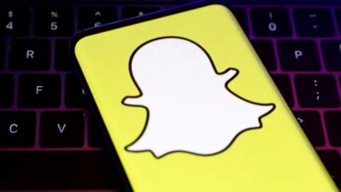 Yellow and wile Snapchat logo on phone screen. With a computer keyboard behind the phone.