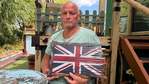 A man holding a very cheaply manufactured wooden flag, which is chipped in one corner