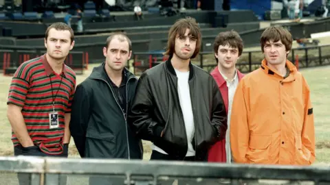 Getty Images Oasis standing together in the audience area at Knebworth in 1996, ahead of the show opening.